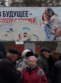Lidé čekají na distribuci humanitární pomoci s proruským billboardem v pozadí po ústupu ruské armády (ilustrační foto)